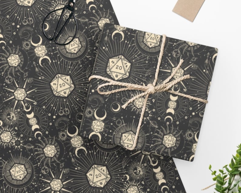 May include: Black and white wrapping paper with a repeating pattern of dice, moons, and suns. The dice are 20-sided and have the number 20 on them. The moons and suns are stylized and have a celestial feel.