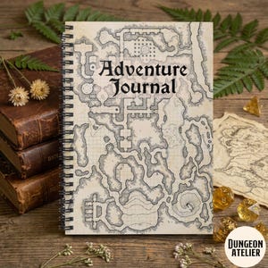 Könnte beinhalten: Ein spiralgebundenes Adventure Journal mit einem detaillierten Kartendesign auf dem Cover. Das Cover zeigt den Text "Adventure Journal" in einer klassischen Schriftart. Das Journal ist von anderen Gegenständen umgeben, darunter Würfel und alte Bücher.