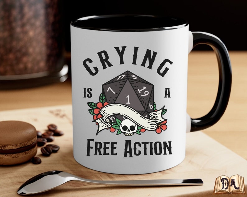 May include: White ceramic mug with a black rim and handle. The mug features a black and white illustration of a twenty-sided die with the text "Crying is a Free Action".