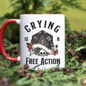 May include: White ceramic mug with a red handle. The mug has a black and white illustration of a 20-sided die with the text "Crying is a Free Action".
