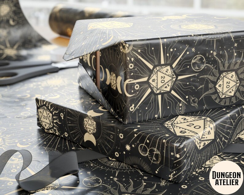 May include: Black and gold wrapping paper with a celestial design featuring dice, moons, stars, and a sun. The paper has the text "Dungeon Atelier" in the bottom right corner.