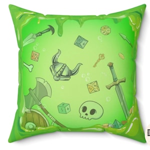May include: Green pillow with a slime-like texture featuring a variety of fantasy-themed illustrations, including a sword, a helmet, dice, and a skull. The pillow has a white border and the text "Dungeon Atelier" in the bottom right corner.