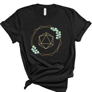 May include: Black t-shirt featuring a gold geometric design with a 20-sided die and eucalyptus leaves. The design is framed by a gold geometric shape. The shirt is made of a soft material.