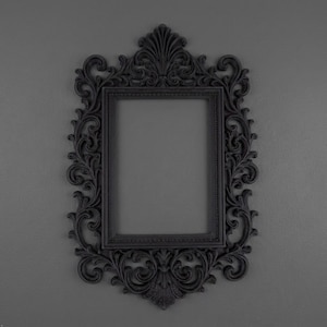 May include: A rectangular picture frame featuring an ornate, matte black finish. The frame is decorated with intricate scrollwork, swirling patterns, and a prominent crest at the top center, surrounding a simple, smooth inner border.