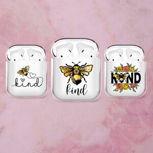 Può includere: Tre custodie bianche per AirPods con disegni di api. Una custodia ha un'ape con un cuore e la parola "kind". La seconda custodia ha un'ape con la parola "kind". La terza custodia ha un'ape con la parola "kind" circondata da fiori.