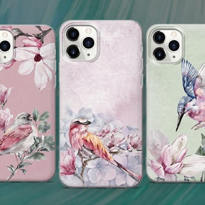 May include: Three phone cases with different floral and bird designs. The first case has a pink background with white magnolia flowers and two birds. The second case has a light pink background with blue and white flowers and a red bird. The third case has a green background with white magnolia flowers and a blue and pink bird.