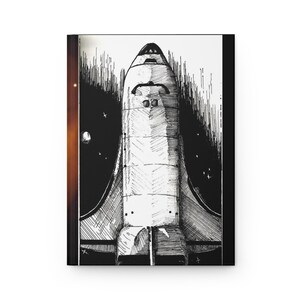 Op de afbeelding: Een notitieboek met een zwart-wit illustratie van een spaceshuttle. De shuttle is gedetailleerd met kruisarcering tegen een sterrenachtergrond. Het notitieboek heeft een witte kaft en een zwarte rug.