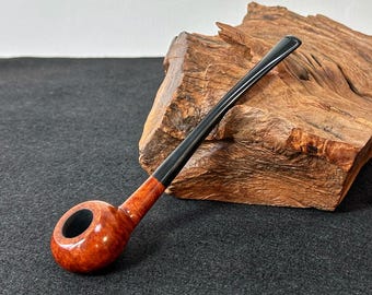 May include: A brown wooden pipe with a black stem. The pipe is resting on a piece of wood.