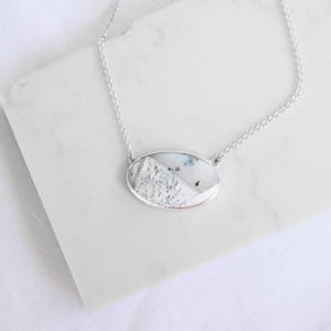May include: A silver chain necklace with a white oval pendant featuring a unique, natural stone pattern.