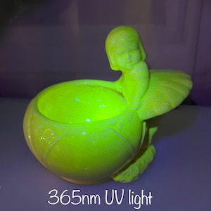 Op de afbeelding: Een vintage, limoengroene keramische figuur van een zittend meisje met een grote, ronde kom. Het beeldje gloeit helder onder 365nm UV-licht. De tekst "365nm UV light" staat onderaan de afbeelding.