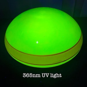 May include: A glowing green sphere with a yellow band around its middle. The text "365nm UV light" is displayed at the bottom of the image. The sphere is illuminated, suggesting it is under a UV light source.