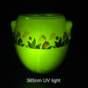 以下が含まれることがあります： 365nmのUVライトの下で光る、花柄の黄色いセラミック製の壺です。