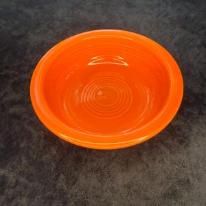 Może przedstawiać: Żywy pomarańczowy ceramiczny talerz o okrągłym kształcie. Miska ma gładkie, błyszczące wykończenie i żebrowane wnętrze. Miska ma jasny, jednolity kolor i prawdopodobnie służy do serwowania potraw.