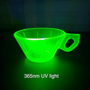 Può includere: Una tazza da tè verde brillante con manico, illuminata da luce UV a 365 nm. La tazza ha una forma triangolare e un manico con un'apertura circolare. Il testo "365nm UV light" è in basso.