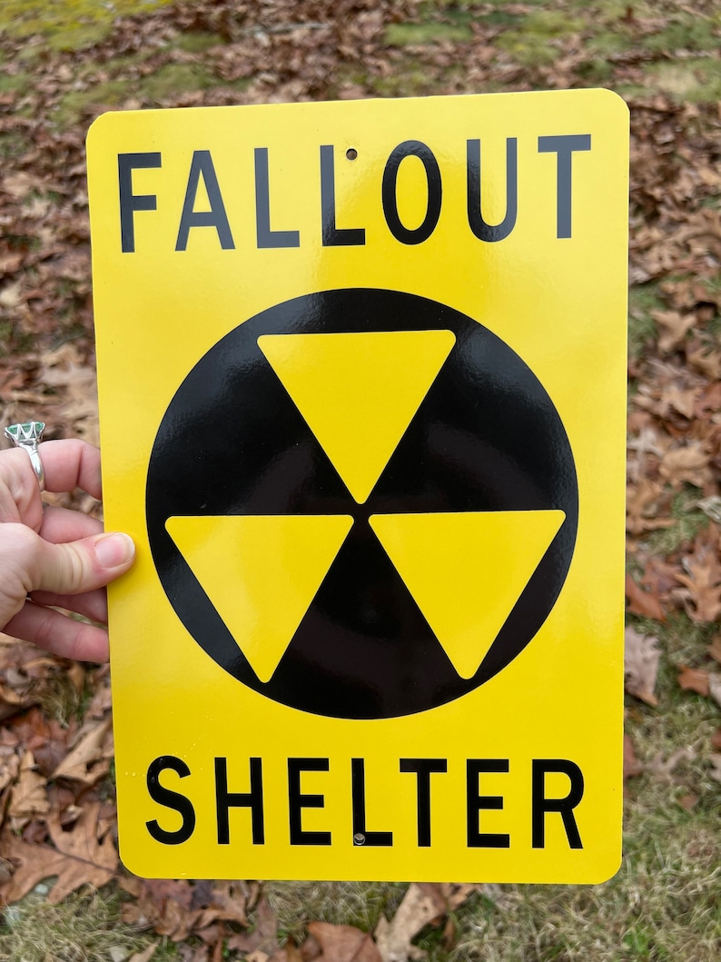 May include: Yellow metal sign with black text that reads "Fallout Shelter" and a black and yellow radiation symbol.