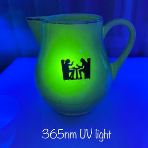 以下が含まれることがあります： ハンドルと注ぎ口が付いた、黄緑色のピッチャー。テーブルを囲む2人の黒いシルエットが特徴です。縁は金色のトリムです。「365nm UV light」の文字が下にあります。