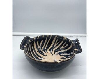 May include: A black and white ceramic bowl with two handles. The bowl has a zebra-like pattern and a dark blue glaze.