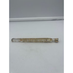 May include: A clear glass bottle with a gold top and a decorative pattern. The bottle is empty and appears to be vintage.