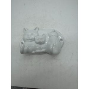May include: White ceramic wall hook with three cats in a row. The cats are in a sitting position and have a simple design.