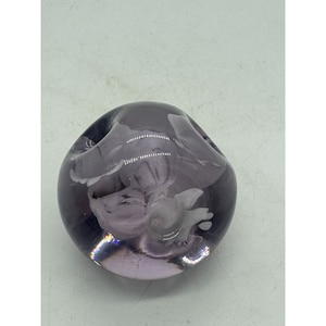 May include: A round, purple glass paperweight with white swirls inside. The paperweight is smooth and shiny.