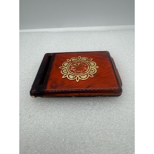 May include: A red and brown cigarette case with a gold floral design.