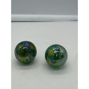 May include: Two iridescent glass spheres with different patterns. One sphere has a swirling pattern, while the other has a speckled pattern. Both spheres are green with hints of blue and gold.