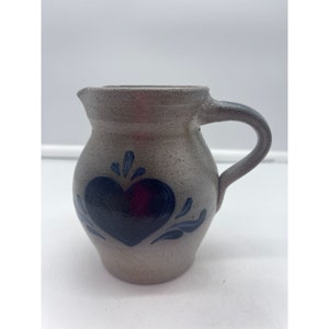 May include: A small gray stoneware pitcher with a blue heart and floral design.