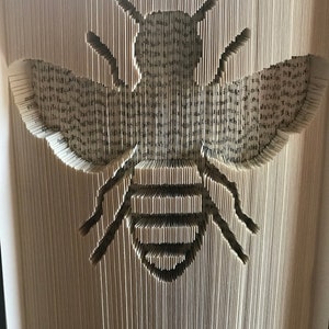 May include: A book art sculpture of a bee, created by folding the pages of a book. The bee is outlined in black and the pages are white.