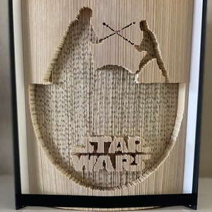 Op de afbeelding: Een boekkunst sculptuur van Star Wars-personages, Luke Skywalker en Darth Vader, die met lichtzwaarden vechten. De sculptuur is gemaakt van de pagina's van een boek, gevouwen en gesneden om de personages en het Star Wars-logo te creëren.