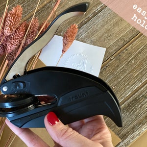 May include: Black self-inking stamp with a silver handle. The stamp has a round impression area and the word "trout" is printed on the side. The stamp is being held in a hand with red nail polish. The text "easy to hold!" is visible in the background.