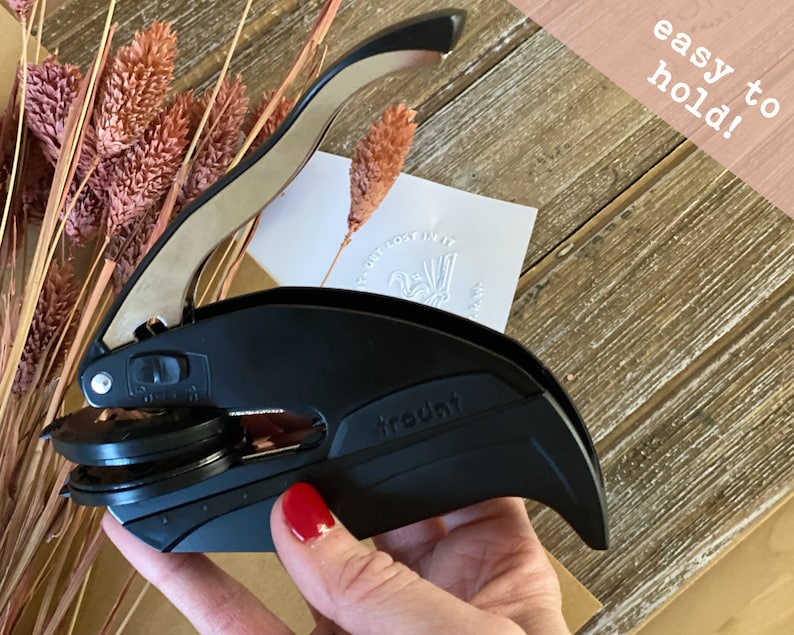 May include: Black self-inking stamp with a silver handle. The stamp has a round impression area and the word "trout" is printed on the side. The stamp is being held in a hand with red nail polish. The text "easy to hold!" is visible in the background.