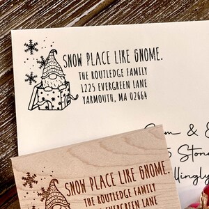 Puede incluir: Un sello de madera con un gnomo en una caja y el texto "SNOW PLACE LIKE GNOME." El texto debajo del gnomo dice "THE ROUTLEDGE FAMILY 1225 EVERGREEN LANE YARMOUTH, MA 02664".
