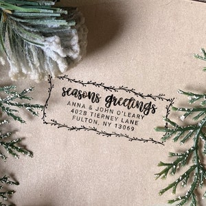Peut inclure: Un tampon d'adresse de retour noir et blanc avec une bordure d&eacute;corative de feuilles et le texte "seasons greetings" et "Anna & John O'Leary, 402B Tierney Lane, Fulton, NY 13069".