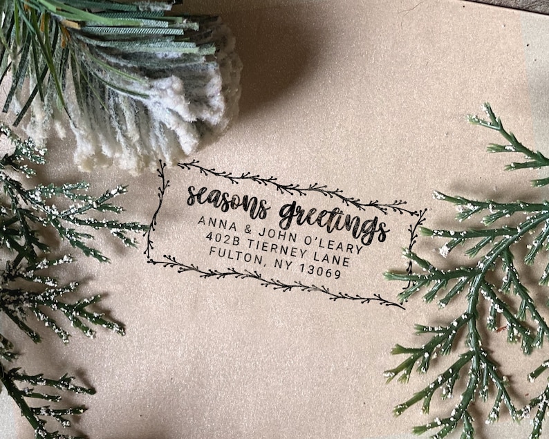 Peut inclure: Un tampon d'adresse de retour noir et blanc avec une bordure d&eacute;corative de feuilles et le texte "seasons greetings" et "Anna & John O'Leary, 402B Tierney Lane, Fulton, NY 13069".