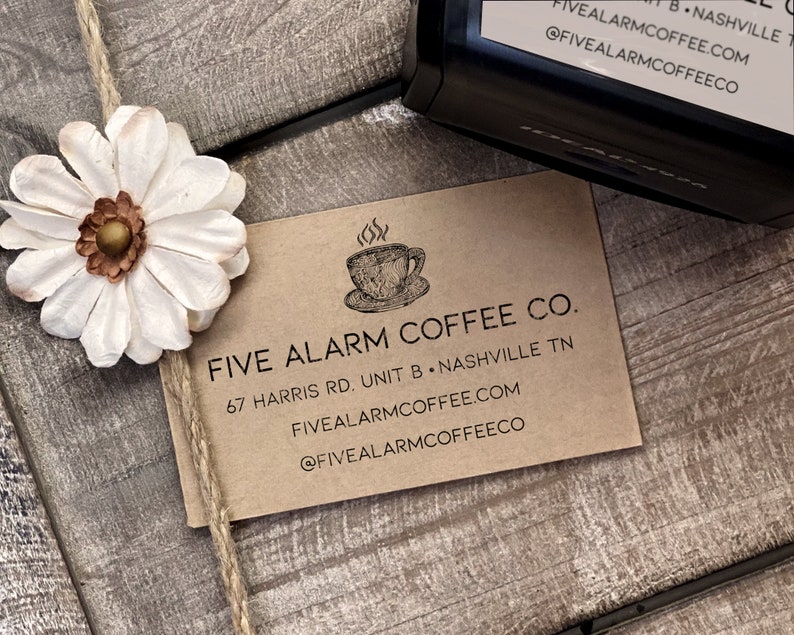 May include: A brown paper business card with the text "Five Alarm Coffee Co." and the address "67 Harris Rd. Unit B, Nashville TN". The card also includes the website "fivealarmcoffee.com" and the social media handle "@fivealarmcoffeeco".