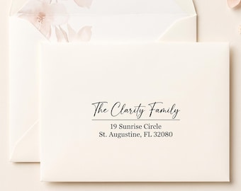 Könnte beinhalten: Ein cremefarbener Umschlag mit schwarzem Aufdruck, der The Clarity Family, 19 Sunrise Circle, St. Augustine, FL 32080 lautet. Der Umschlag liegt vor einem weiteren Umschlag mit einem zarten Blumenmuster.