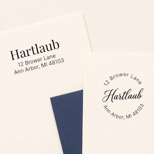May include: Two white paper cards featuring black ink return address stamps. One card displays the name Hartlaub with the address 12 Brower Lane, Ann Arbor, MI 48103 in a serif font. The other shows the same text in a circular layout.