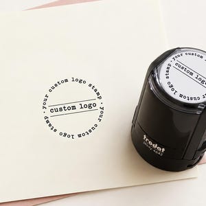 Pode incluir: Um carimbo autoentintado preto Trodat Printy 4642 com uma área de impressão circular. O carimbo apresenta o texto 'custom logo' no centro com 'your custom logo stamp' escrito em um círculo ao redor do perímetro em papel branco.