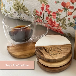 Könnte beinhalten: Satz mit vier runden Holz-Untersetzern mit einer weißen Marmorplatte. Die Untersetzer haben ein personalisiertes Design mit den Initialen "R&S" und dem Text "The  Snyders".