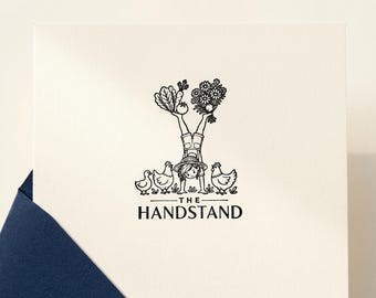 May include: A square off-white greeting card featuring a black ink illustration of a person in a handstand wearing a hat and overalls. The person balances vegetables and flowers on their feet, surrounded by three chickens. Text reads THE HANDSTAND.