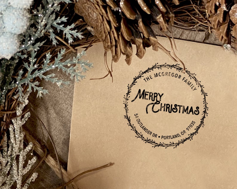 Peut inclure: Une carte en papier brun avec un tampon d'encre noire qui indique "The McGregor Family Merry Christmas 54 Outlander Dr. Portland, OR 97035" dans un design de couronne.