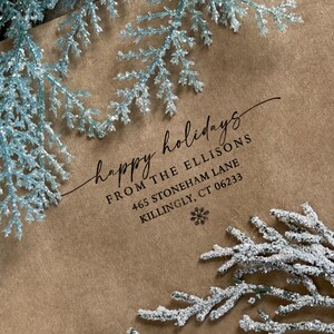 Peut inclure: Une enveloppe en papier brun avec un flocon de neige blanc et le texte "happy holidays" en cursive. Le texte "From The Ellisons 465 Stoneham Lane Killingly, CT 06233" est imprim&eacute; sous le message.