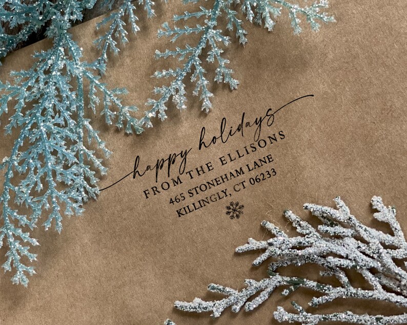 Peut inclure: Une enveloppe en papier brun avec un flocon de neige blanc et le texte "happy holidays" en cursive. Le texte "From The Ellisons 465 Stoneham Lane Killingly, CT 06233" est imprim&eacute; sous le message.