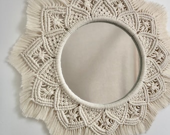 Peut inclure: Miroir macramé crème avec un miroir central rond. Le design macramé présente des nœuds complexes et une forme d'étoile avec des bords à franges. Une décoration murale.
