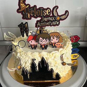 Könnte beinhalten: Ein runder Kuchen mit weißem Zuckerguss und dekorativen Aufsätzen. Die Aufsätze zeigen Cartoon-Figuren, eine Schlosssilhouette und den Text "Heloise Joyeux Anniversaire". Goldene Schnatze und eine Brille sind ebenfalls vorhanden.