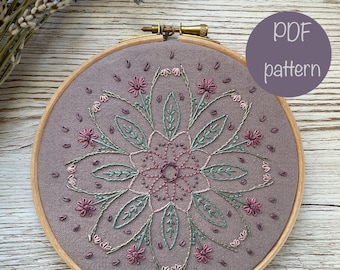 May include: A floral embroidery pattern in a hoop. The design features a mandala with pink and green flowers and leaves on a light brown fabric.