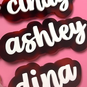 May include: Five personalized keychains with names: "erica", "steph", "cindy", "ashley", and "dina". Each keychain features a tortoiseshell-patterned base with a white, cursive name. Gold-colored key rings and clasps are attached to each keychain.