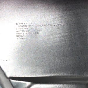 May include: Close-up of a silver metal baking pan with text that reads "&copy; 1983 PEYO LICENSED BY WALLACE BERRIE & CO., INC VAN NUYS, CA WILTON ENTERPRISES WOODRIDGE, IL 60517 KOREA 502-4033."