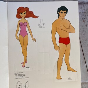 May include: A paper doll set featuring Ariel and Eric from the Disney film The Little Mermaid. Ariel is wearing a pink swimsuit and Eric is wearing red swimming trunks. The dolls are printed on white paper and have instructions for assembly.