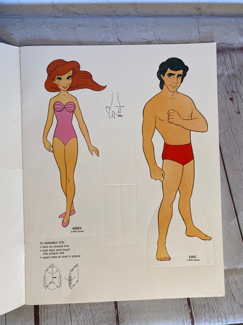 May include: A paper doll set featuring Ariel and Eric from the Disney film The Little Mermaid. Ariel is wearing a pink swimsuit and Eric is wearing red swimming trunks. The dolls are printed on white paper and have instructions for assembly.